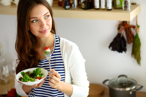 Young woman eating salad and holding a mixed salad